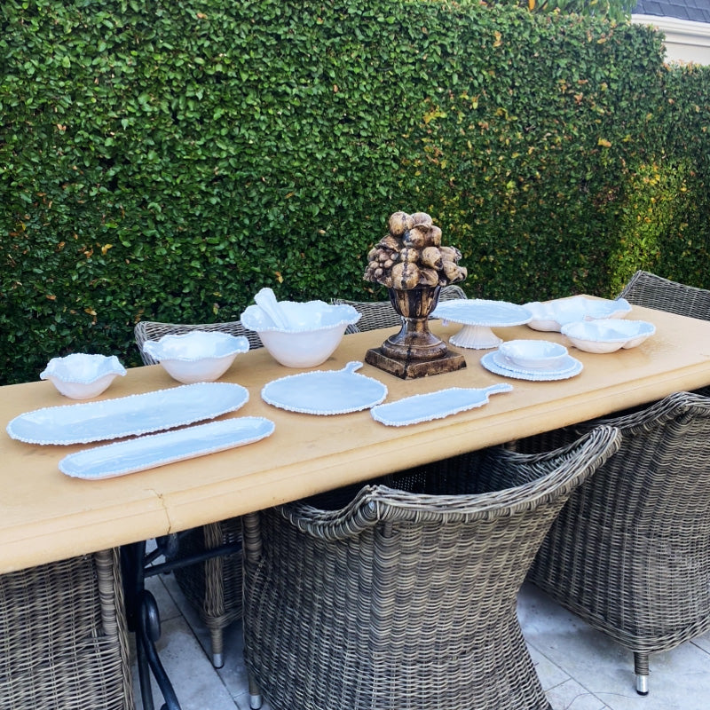 Outdoor table setting with a range of white ceramic serveware, rattan seats and hedges