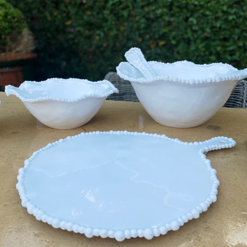 White platter and set of bowls with pearl edges on an outdoor table