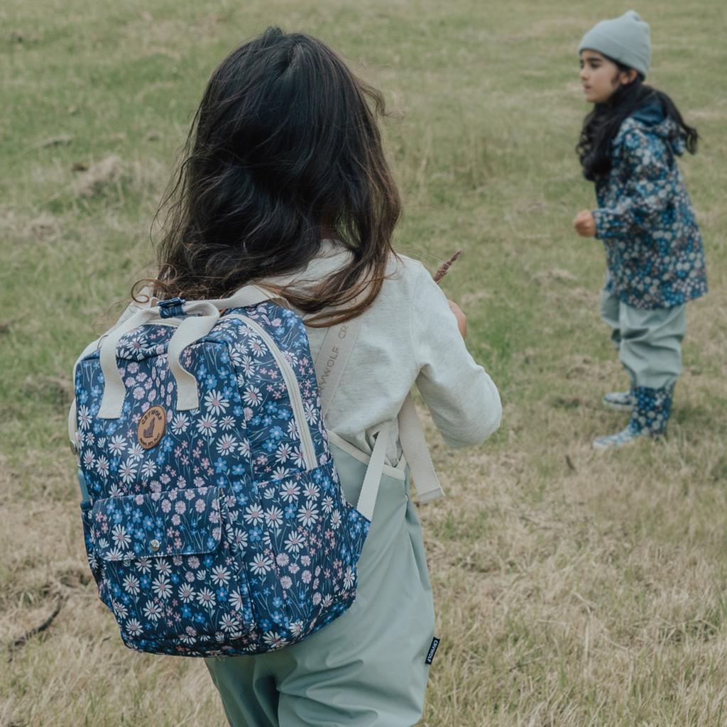 A young girl walking through a grassy field, wearing casual clothing and enjoying the outdoors with another child in the forgreound