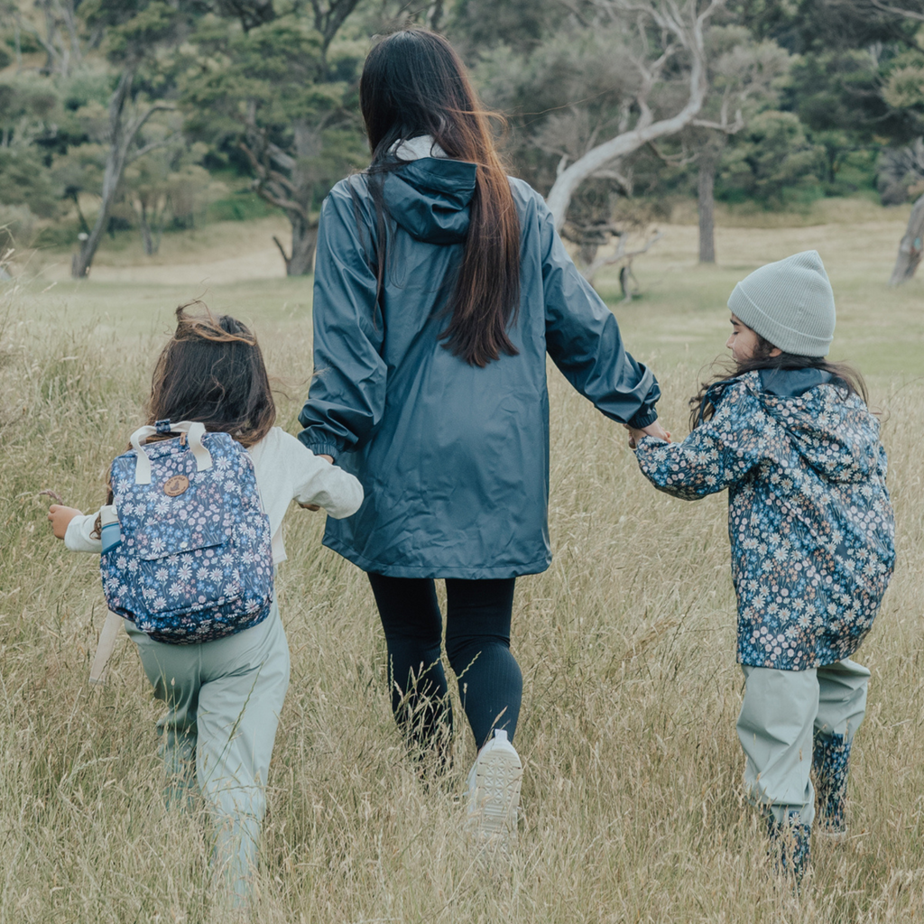 A woman holding hands with two kids walking outdoors in a field