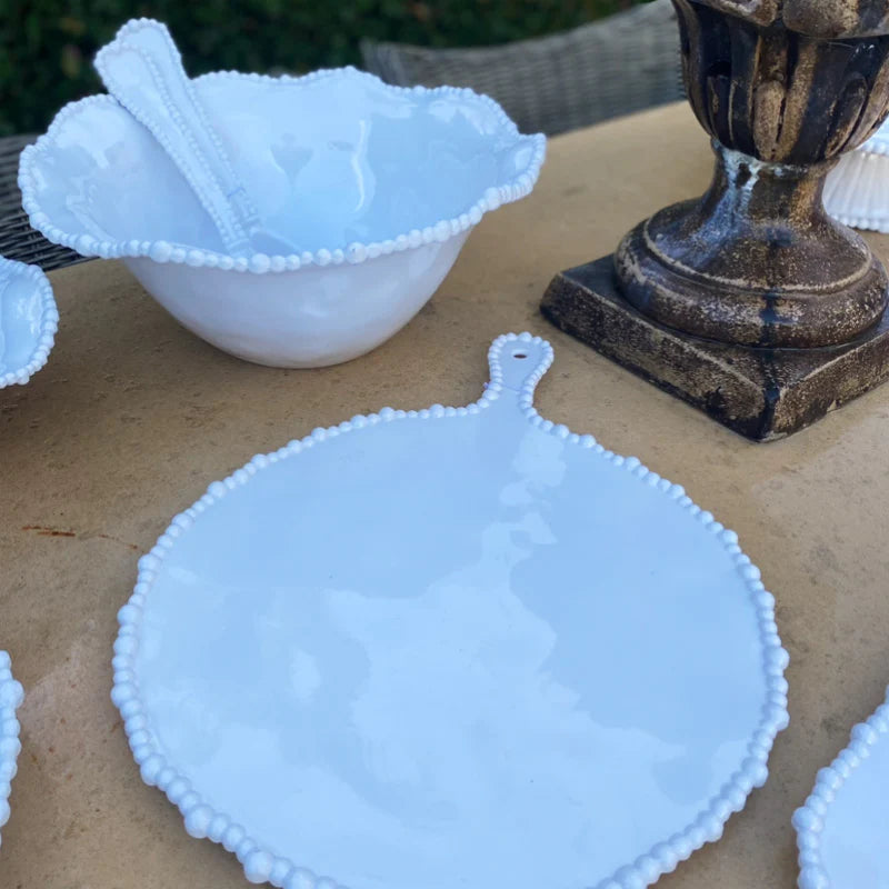 White bowl and platter with serving spoons and a candle stick upon an outdoor table