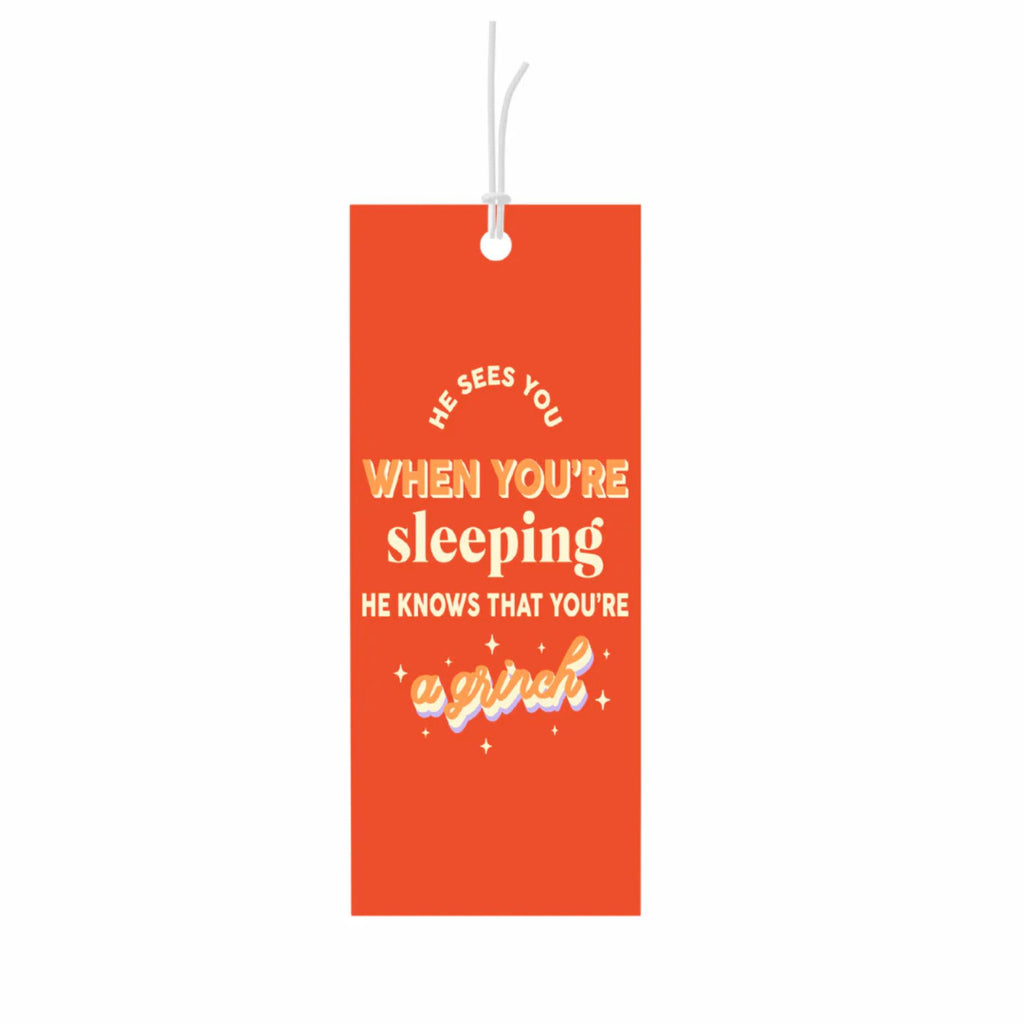 Red gift tag reading "he sees you when you're sleeping he knows that you're a grinch" in orange and white text