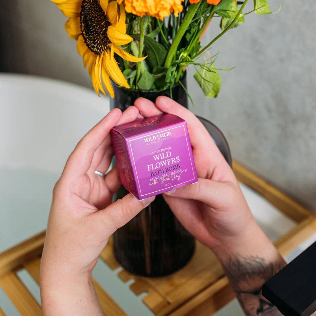 Bath Bomb - Wild Flowers by Wild Emery.  A bright pink box showing hands holding the box and sunflowers in the background