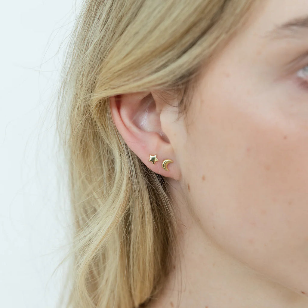 Woman wearing a gold stud earring set of one star shape and one moon shape