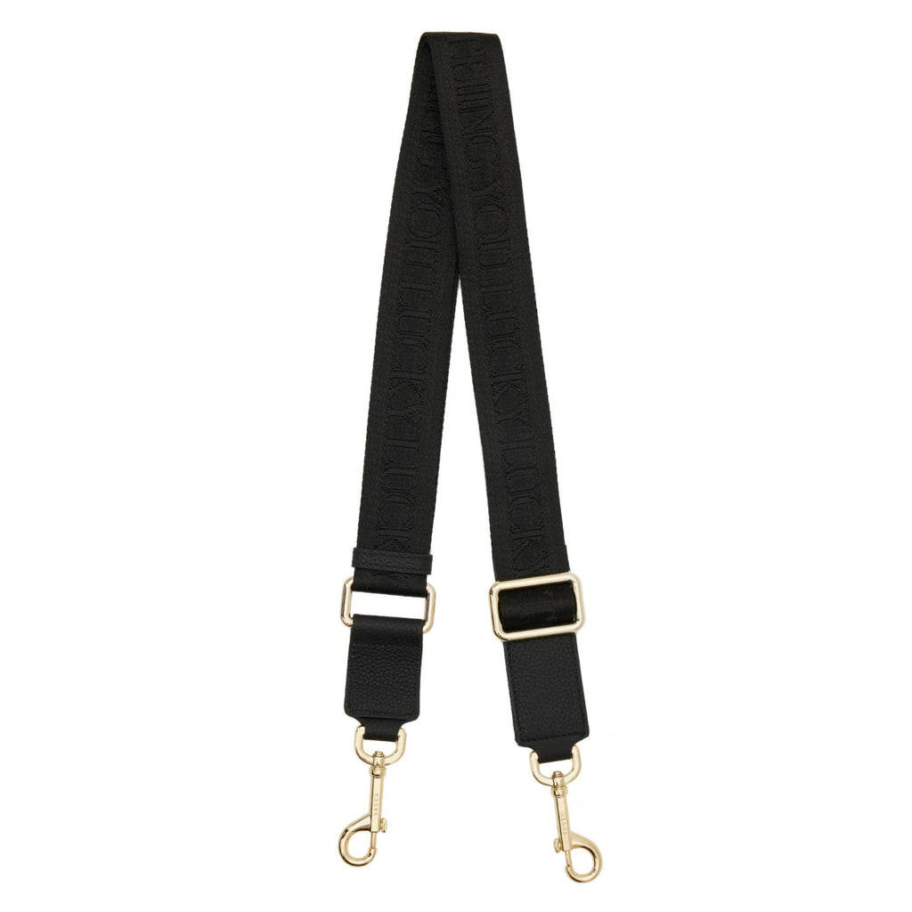 A white background with thick black cotton fabric bag strap with gold hardwear and clips on the end.