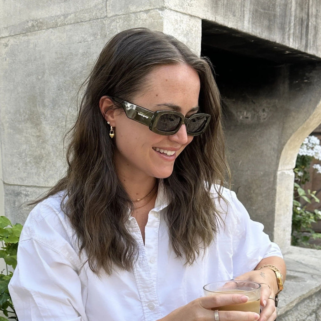 A woman drinking a coffee outside in sunglasses and a blouse