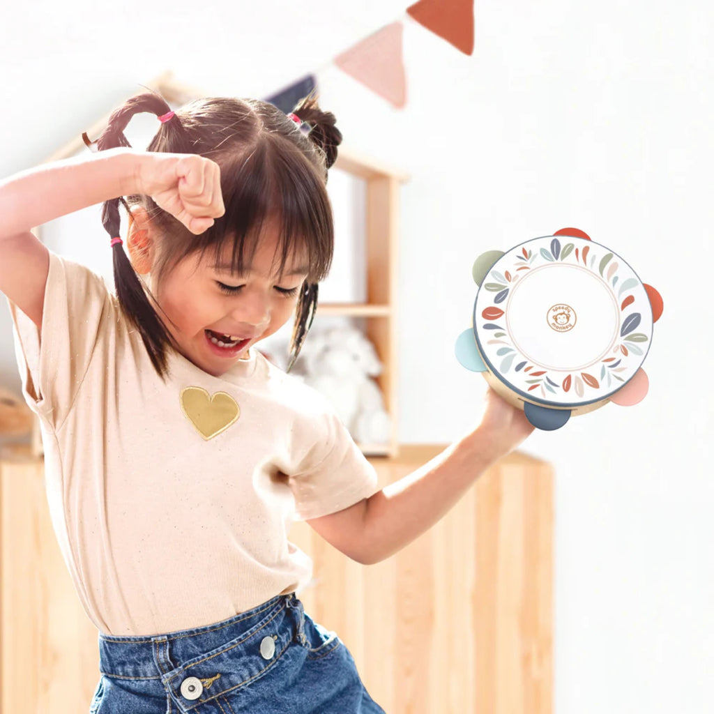 A young girl playing indoors with a toy tambourine