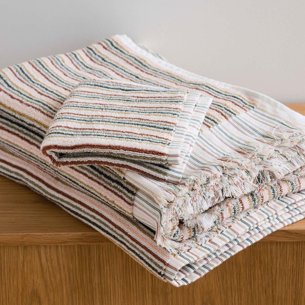 A folded set of two towels and a washcloth on a wood cupboard in a multi-coloured stripe pattern 