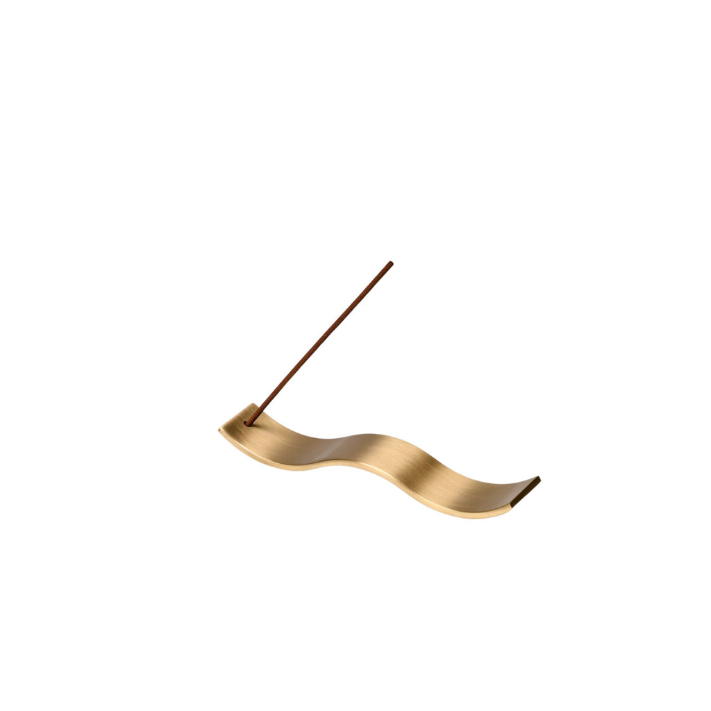 A gold wave incense holder with a stick of incense