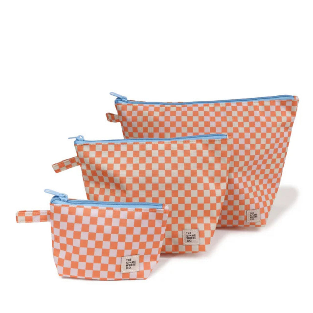 white background with a set of three cosmetic pouches in three sizes in the foreground. Orange and white checkered with blue zips