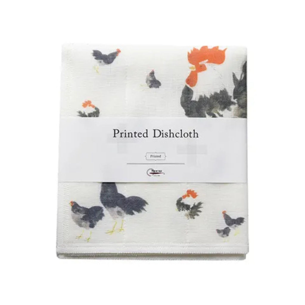 Folded dishcloth with a labeled sleeve. Against a white background. Dishcloth has roosters and hens illustrated on it.