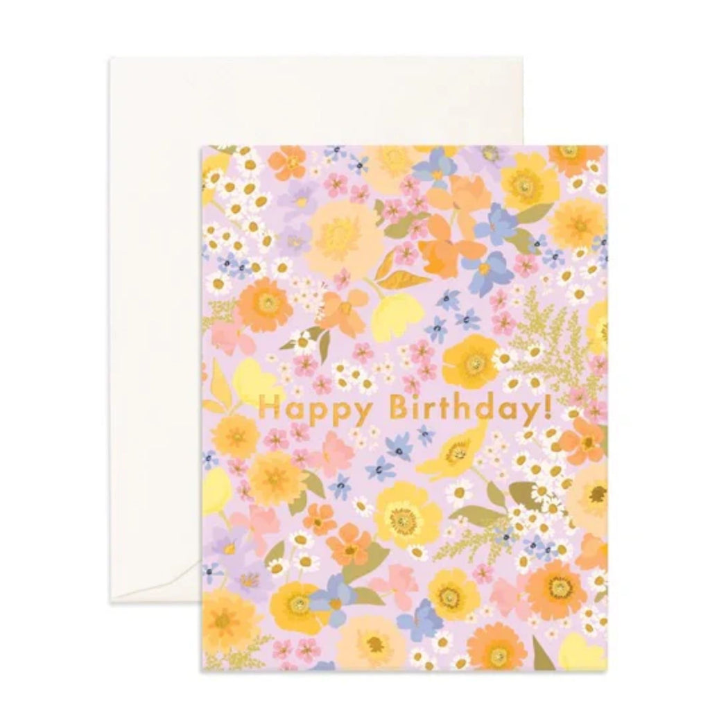 Light pink greeting card with flowers and foliage on it reading "happy birthday" in gold text with an envelope