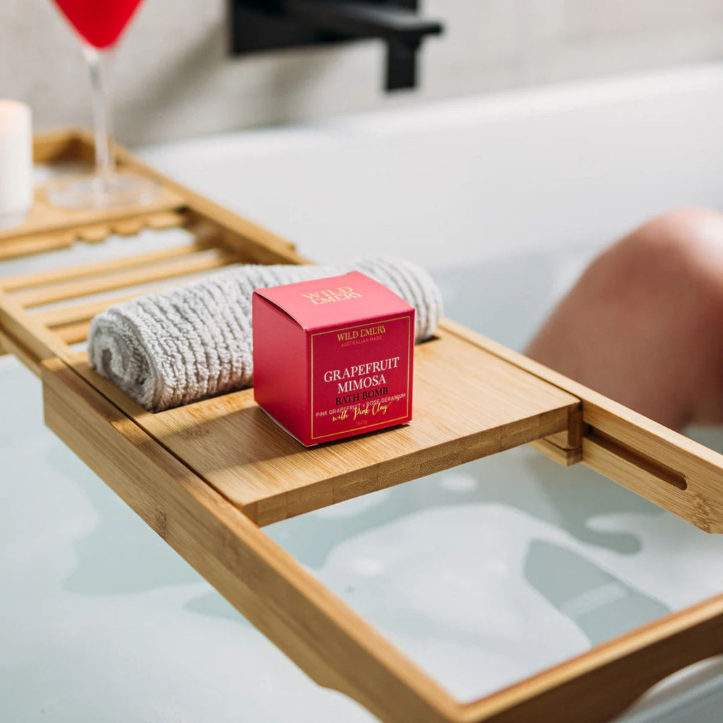 Bath Bomb - Grapefruit Mimosa by Wild Emery. Red packaging box sitting on a wooden shelf over bathtub