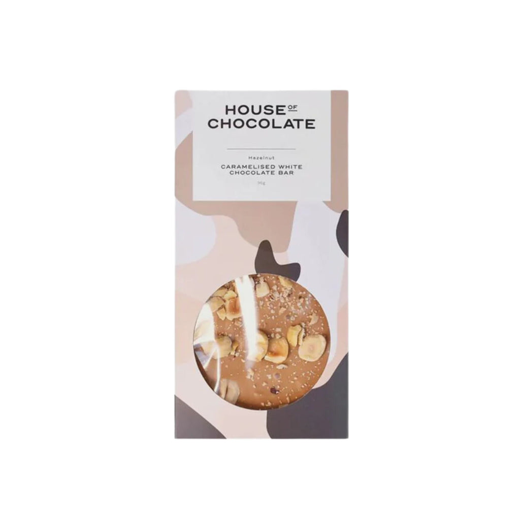 A caramelised white chocolate bar with hazelnut topping in a brown, pink and white splotch package labelled "house of chocolate" with the subtitle "Hazelnut caramelised white chocolate bar" against a white background