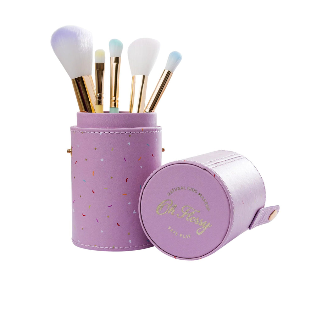 A purple leather cylinder case holding 5 makeup brushes with a top of the case lying next to it with a confetti pattern and Oh Flossy gold branding against a white background 