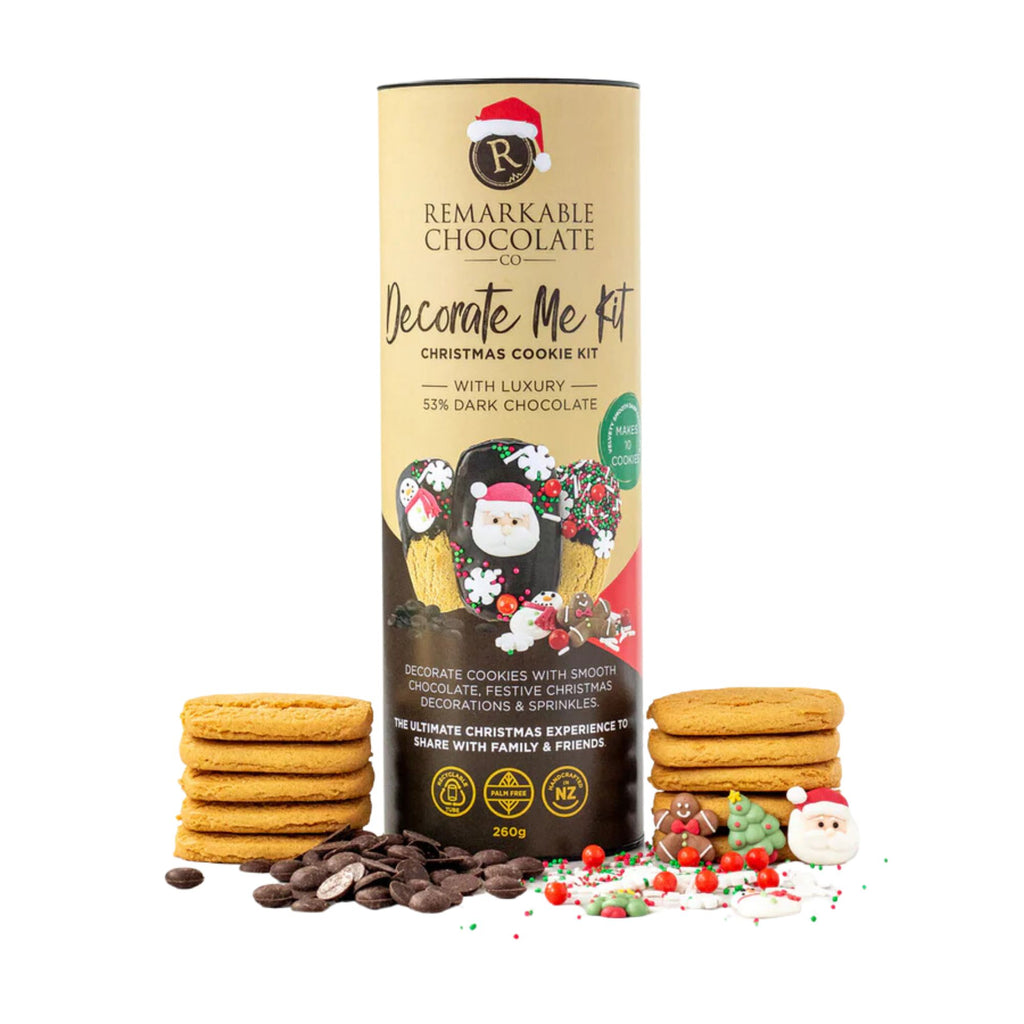 A tube shaped box of decorative Christmas cookies labeled "Remarkable Chocolate - Christmas Cookie Kit" featuring 53% dark chocolate, with decorations for cookies including festive sprinkles and the tagline "The ultimate Christmas experience to share with family & friends" with an assortment of cookie stacks and cookie decorating toppings surrounding it.