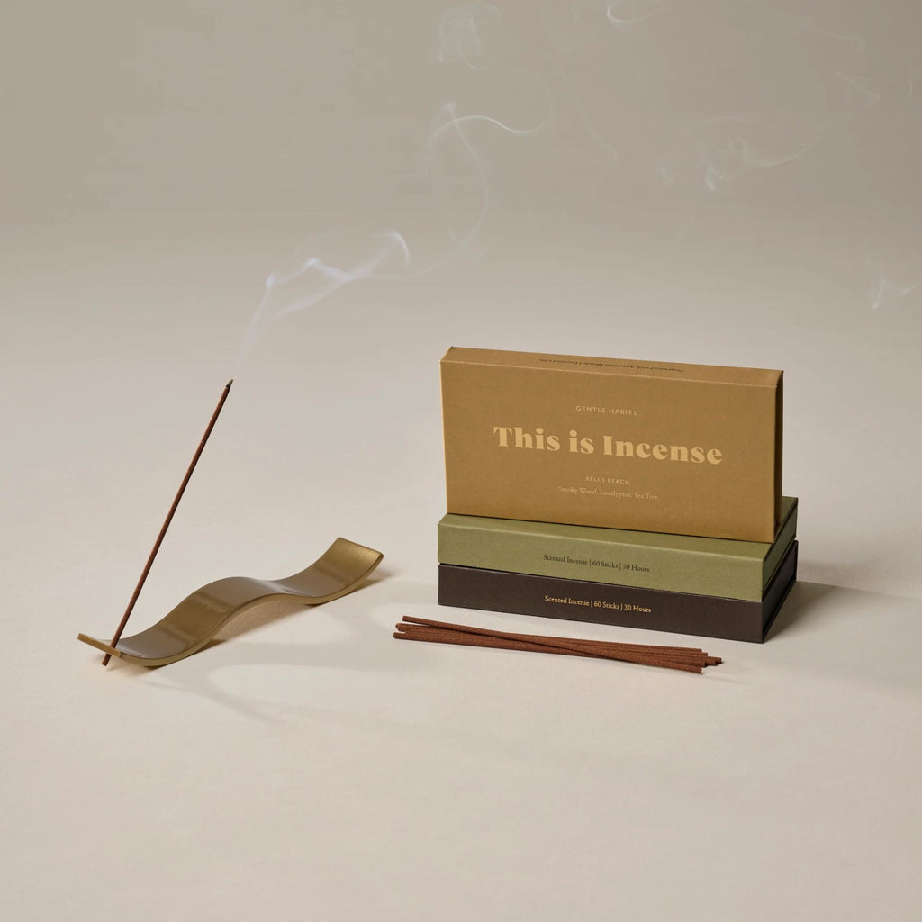 A gold wave incense holder with a stick of incense, 3 boxes of incense and a pile of incense sticks