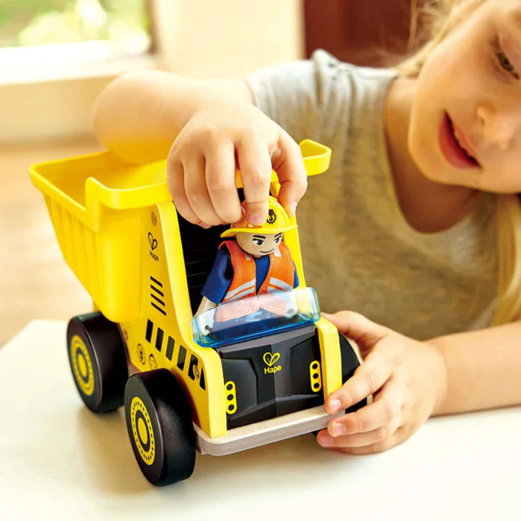 Girl playing with yellow toy dump truck and driver figure