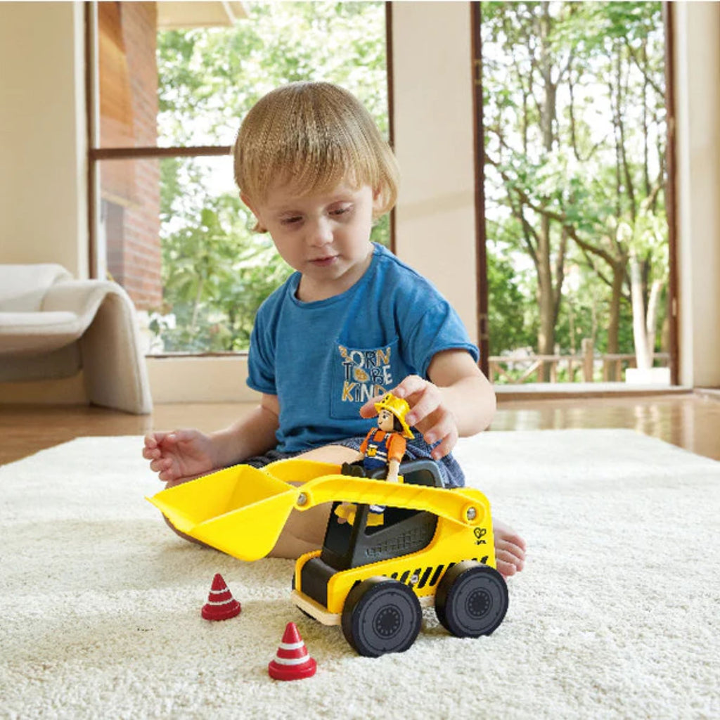 Boy playing with yellow toy loading truck, construction person figure and 2 red cones