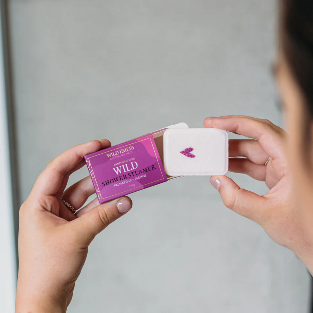 Person in shower pulling a white shower steamer out of a purple box labeled wild