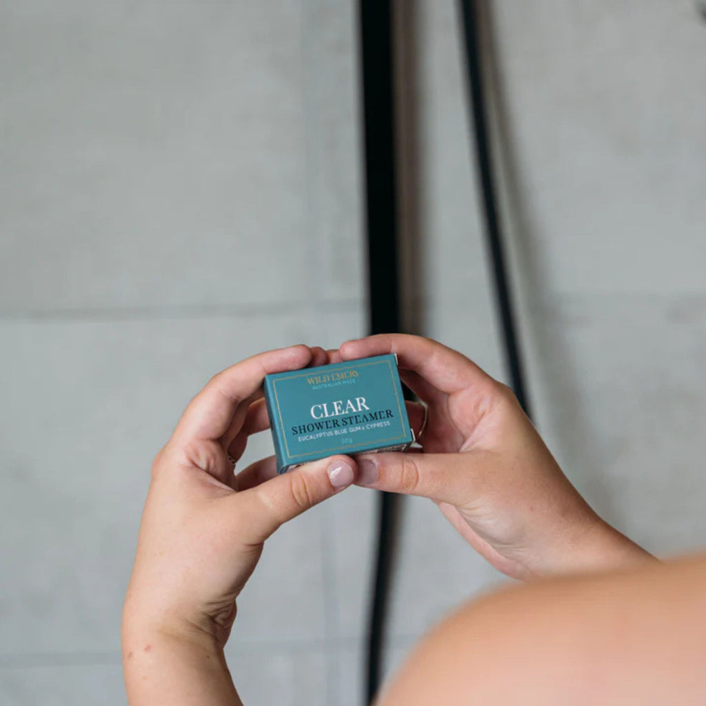 Person in shower holding a turquoise shower steamer box in scent clear