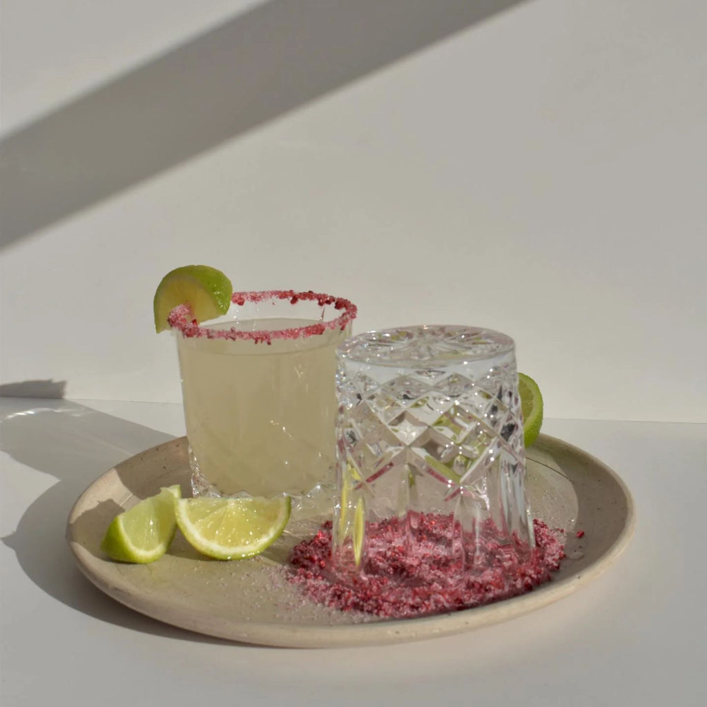 A margarita and an upside down glass on a plate with limes and pink rim dust