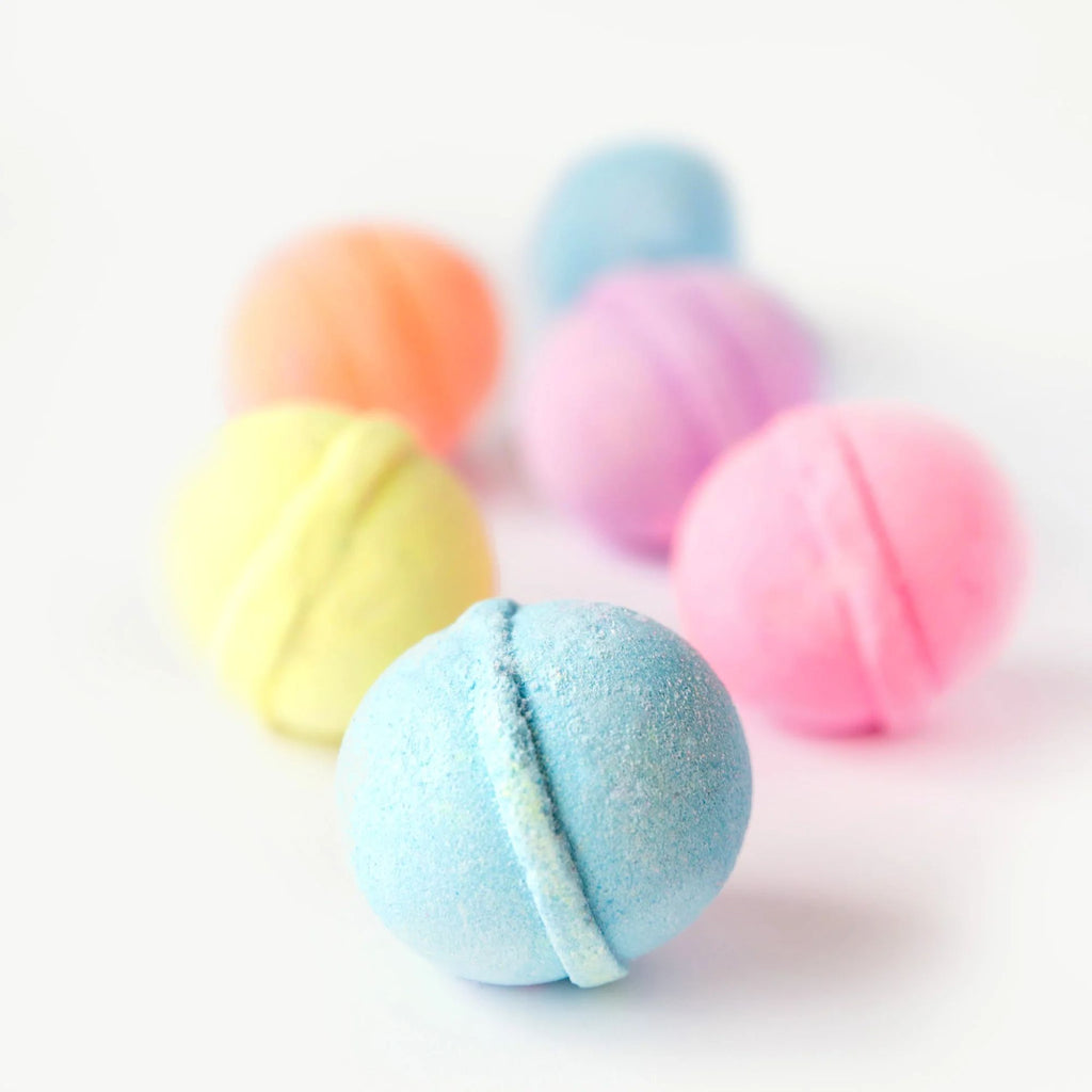 A set of 6 bath bombs in various colours with 5 of the bath bombs out of focus in the foreground against a white background. 