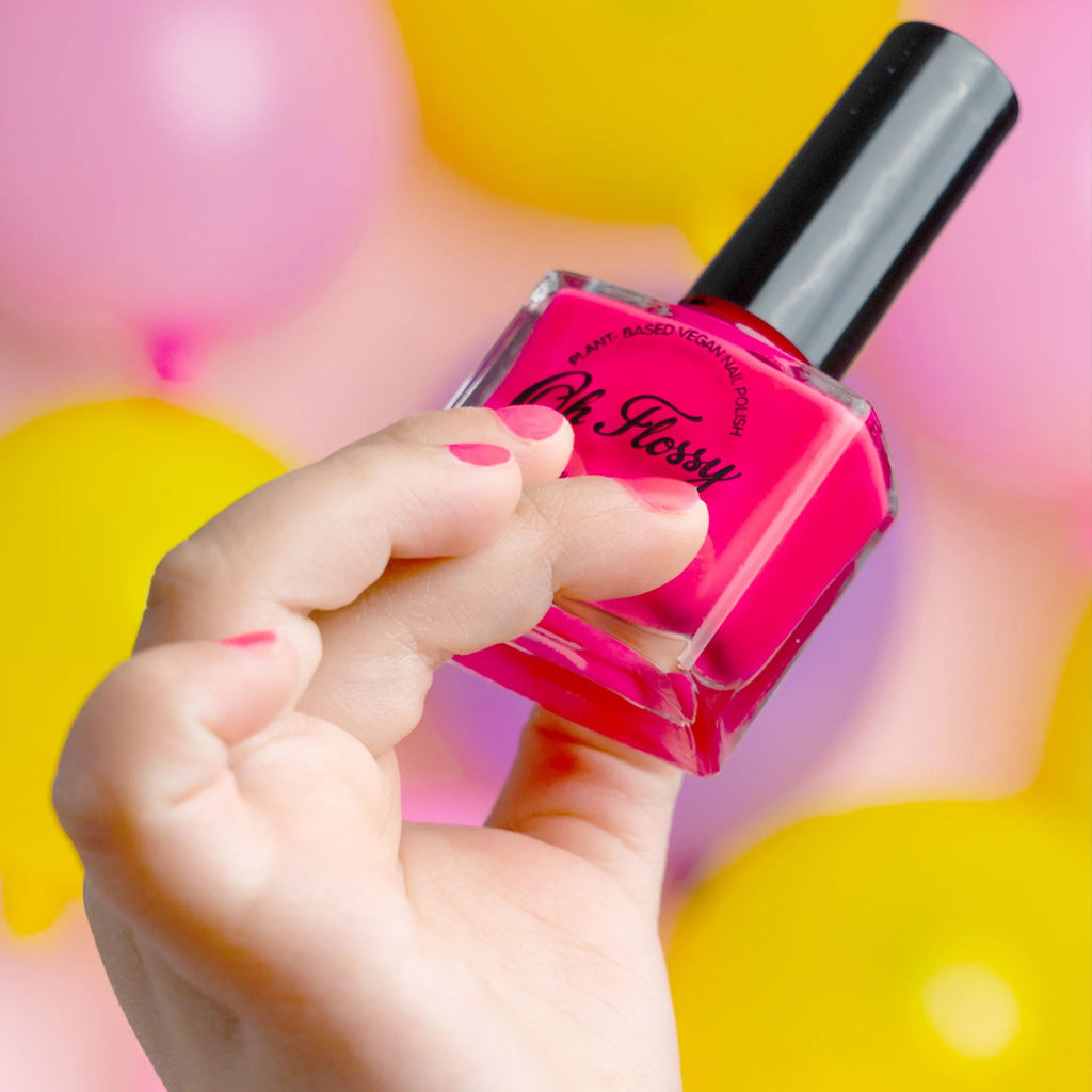 A picture of a blurred  yellow background 
 with balloons and a girl with a focused hand holding a bottle of pink nail polish with painted nails.