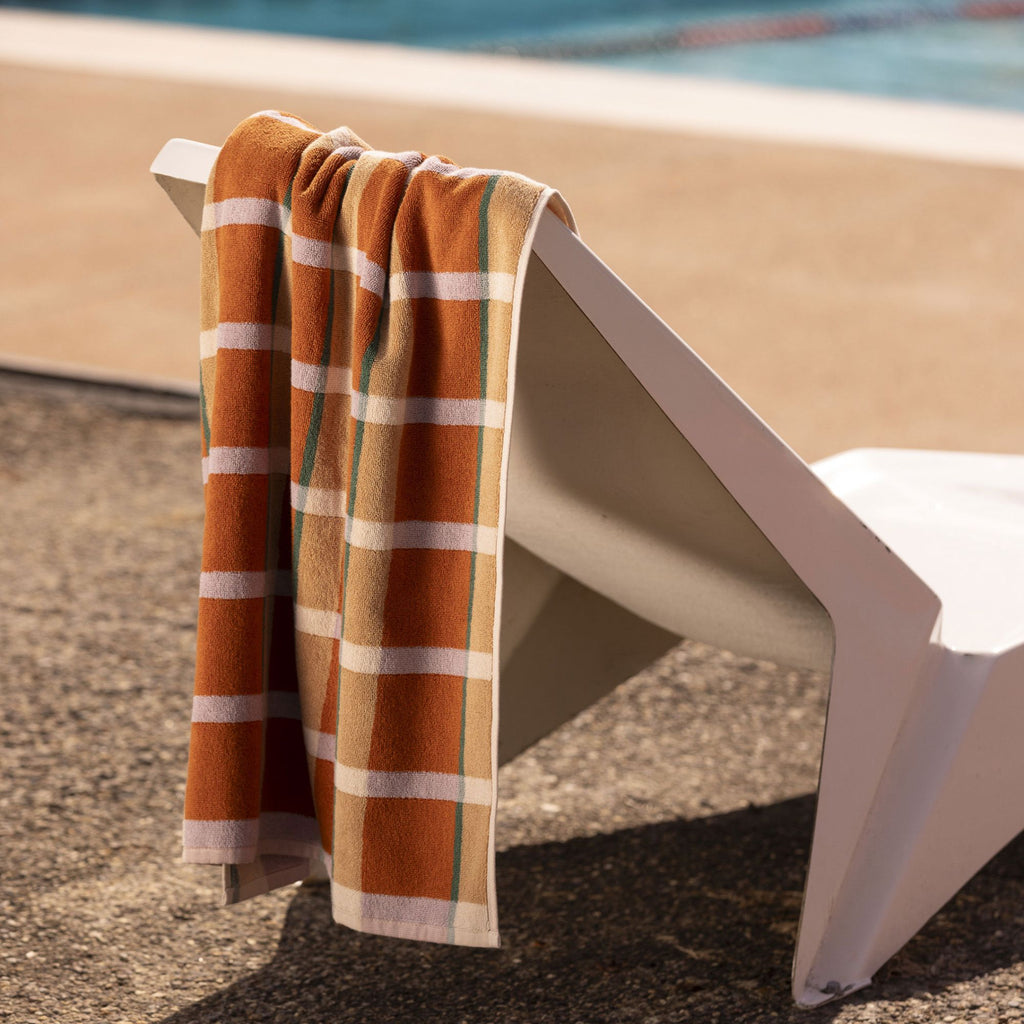 Multicoloured orange check towel resting on a white lounger chair poolside on concrete