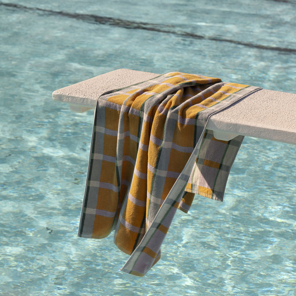 A Yellow, blue and green check patterned beach towel resting on a diving board above a pool