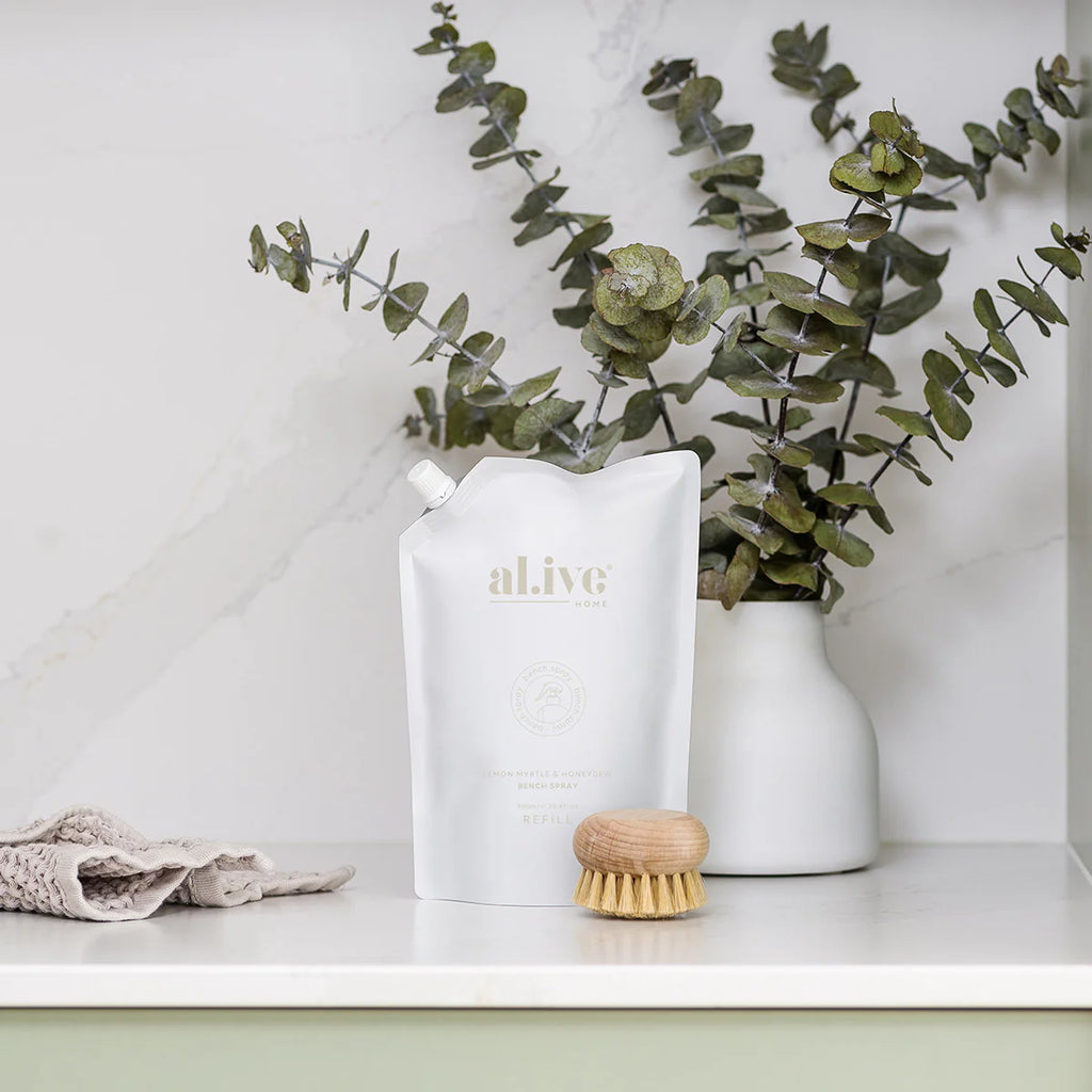 White pouch of bench spray on a bench with a scrubber, tea towel and vase