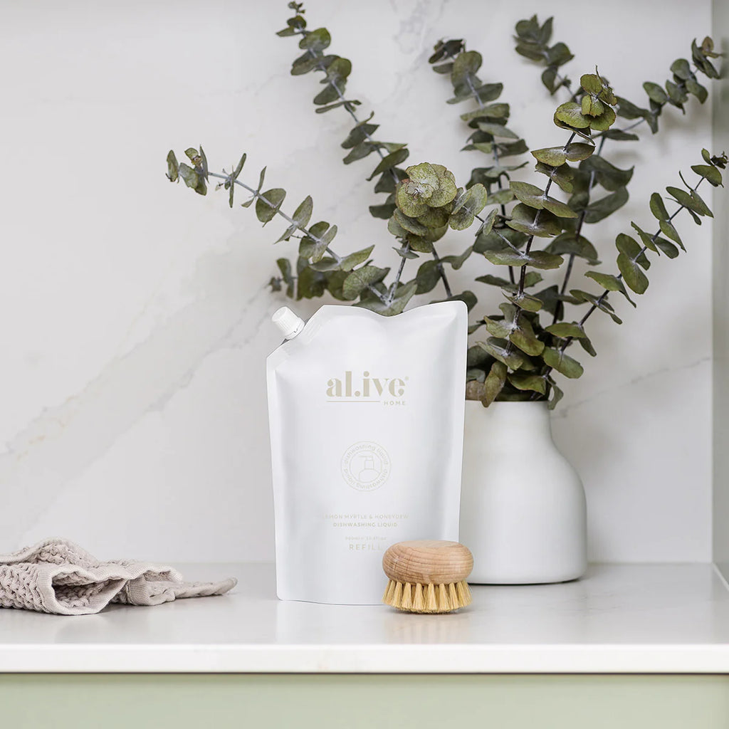 White pouch of dishwashing liquid on kitchen bench with scrubber, tea towel and a vase